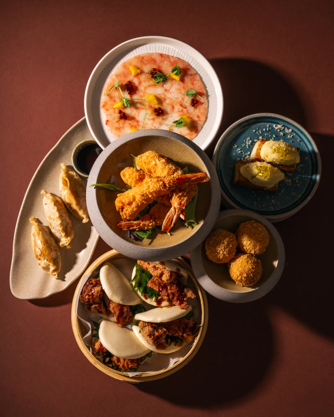 La tavola vista dall'alto: carpaccio di gambero rosso, gyoza, tempura di mazzancolle, shokupan, polpette di ricciola e bao al vapore